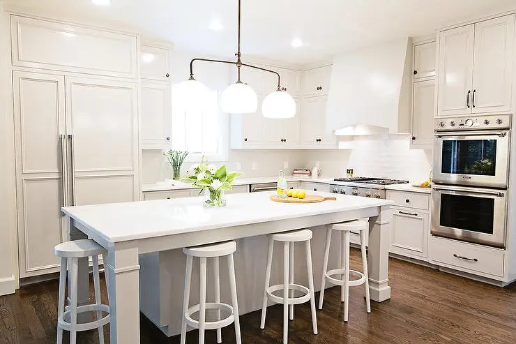 A kitchen with white Worktable Island and backless metal stools