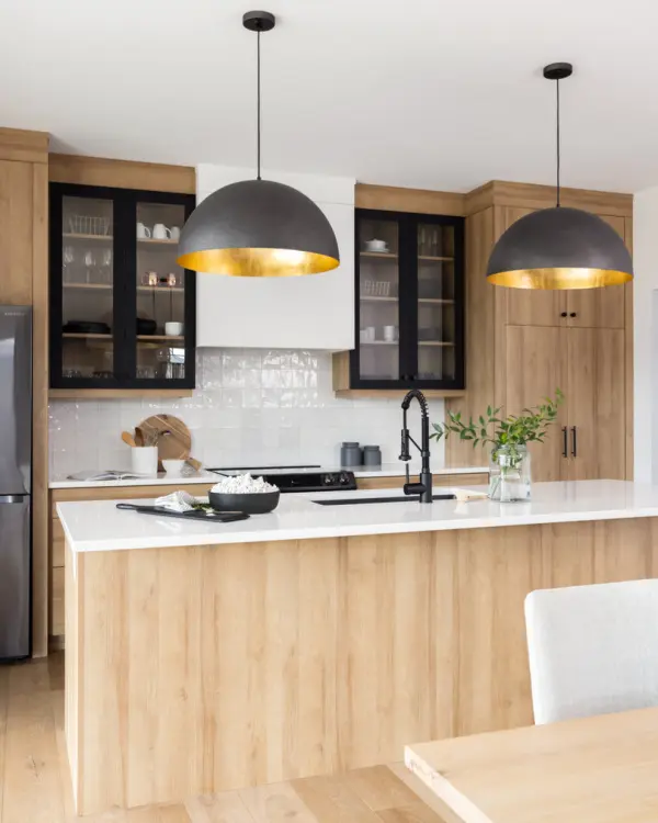 A beautiful kitchen with the black pendant lights and black frames on the glass cabinets in contrast with wooden cabinets.