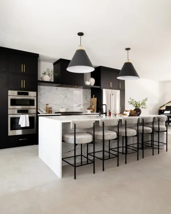 A classy and beautiful kitchen with all-black cabinets reaching the ceiling with a light-colored quartz and matching backsplash with the stark white walls.