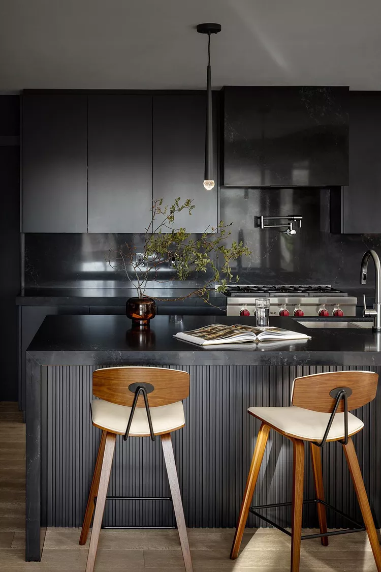 A classy kitchen with matte black cabinets and a glossy black backsplash of stone